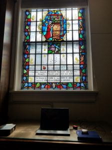 Graduate Assistant Desk and laptop. Stained glass window depicting Robert Browning's Ferishtah's Fancies above desk. 