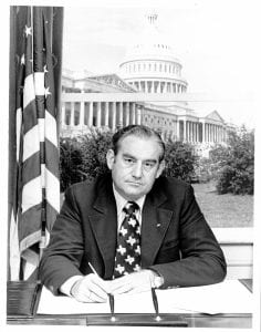 Photo of Texas Representative Sam Hall seated at his desk with US Capitol Building behind.