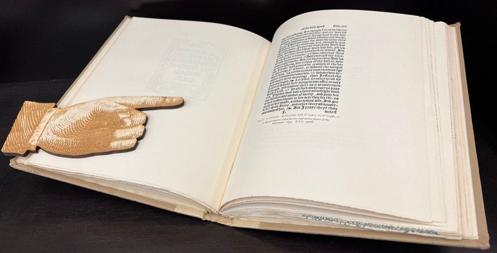 Open book containing a manicule being held open by a laser-cut manicule
